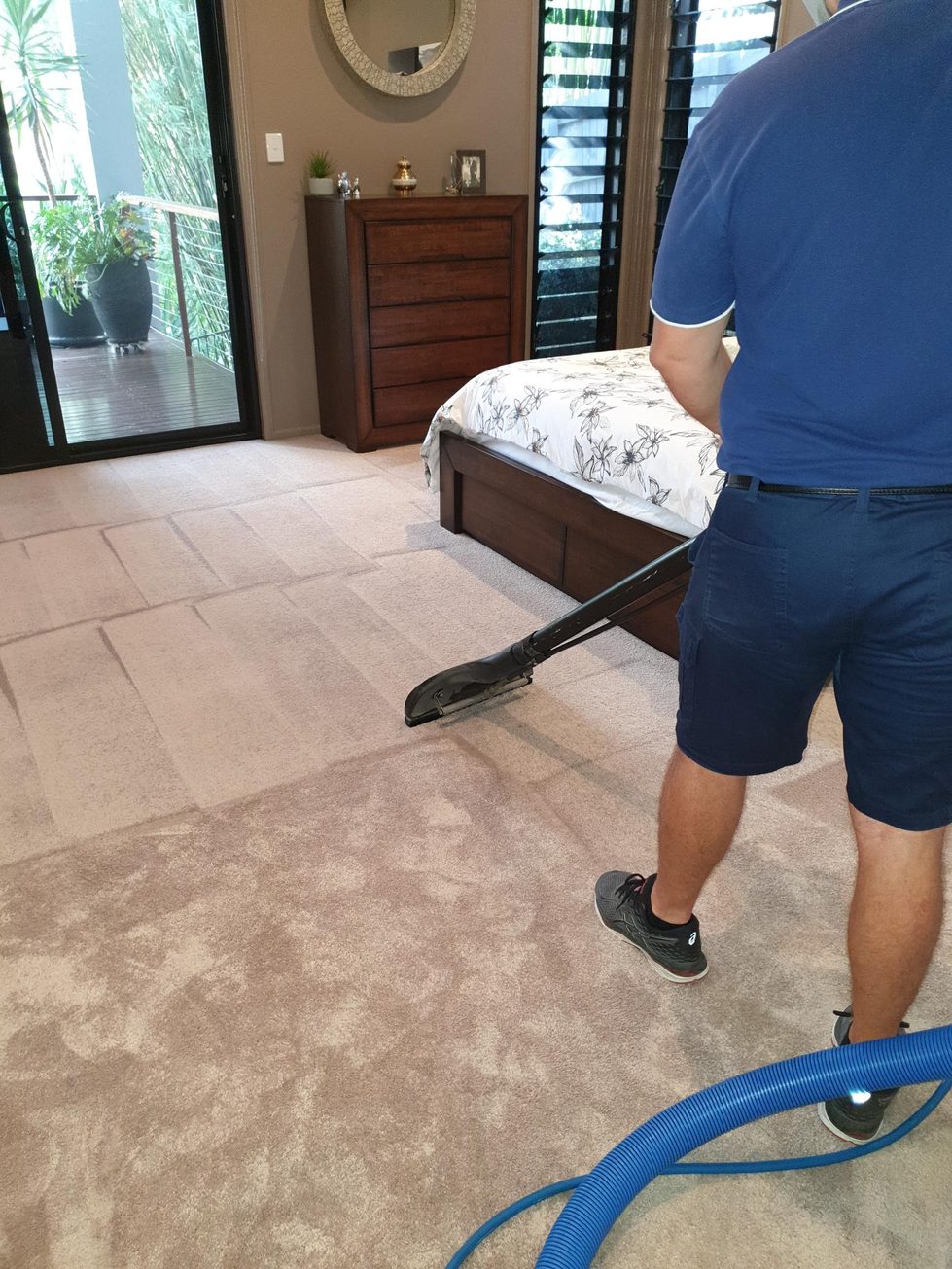 Nu-Look technician cleaning bedroom carpet right up to the bed and chest of drawers, with the cleaned strip clearly lighter