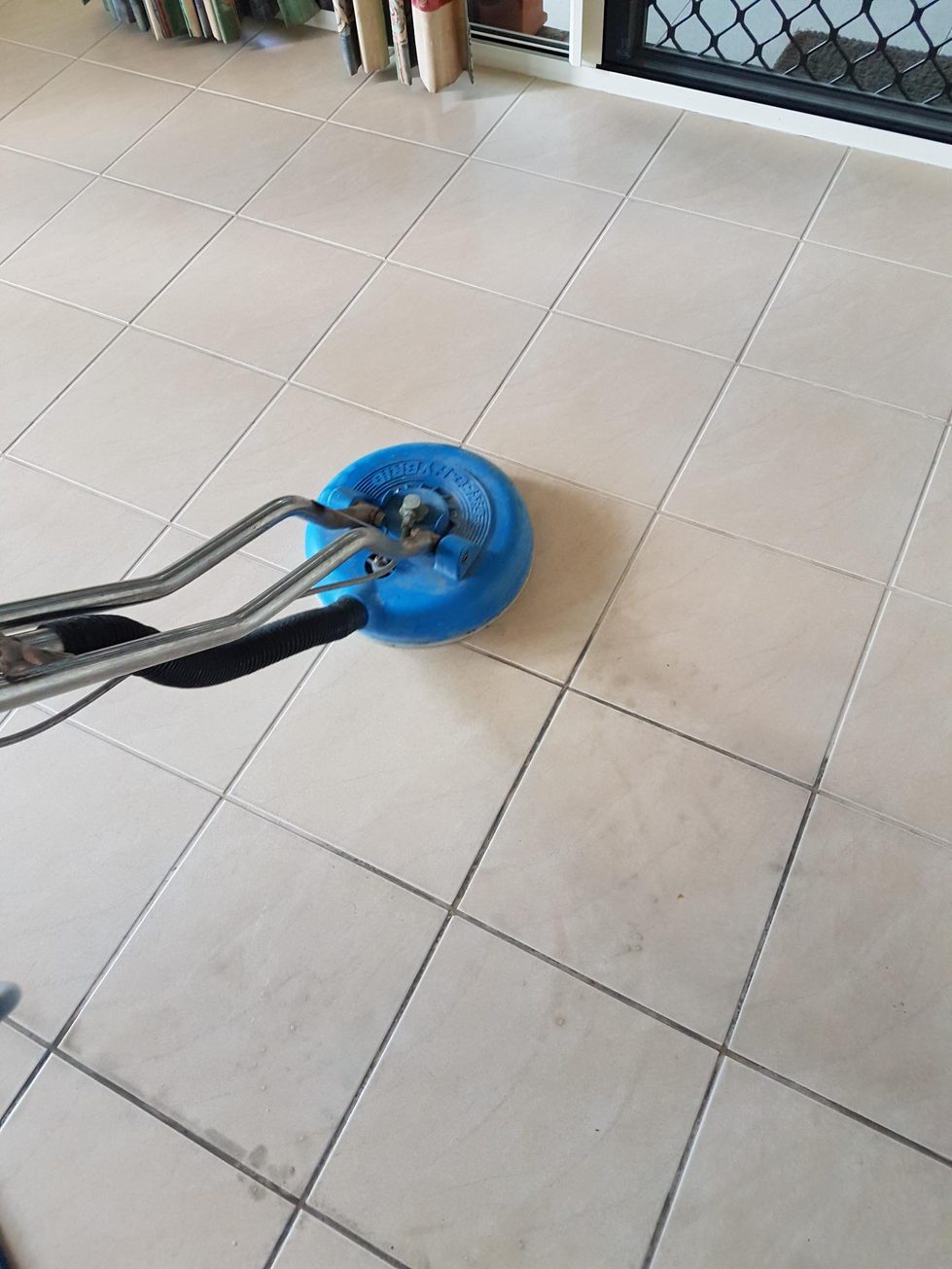 Truck-mounted rotary tile cleaning head part-way across a tiled floor, the cleaned tiles clearly lighter