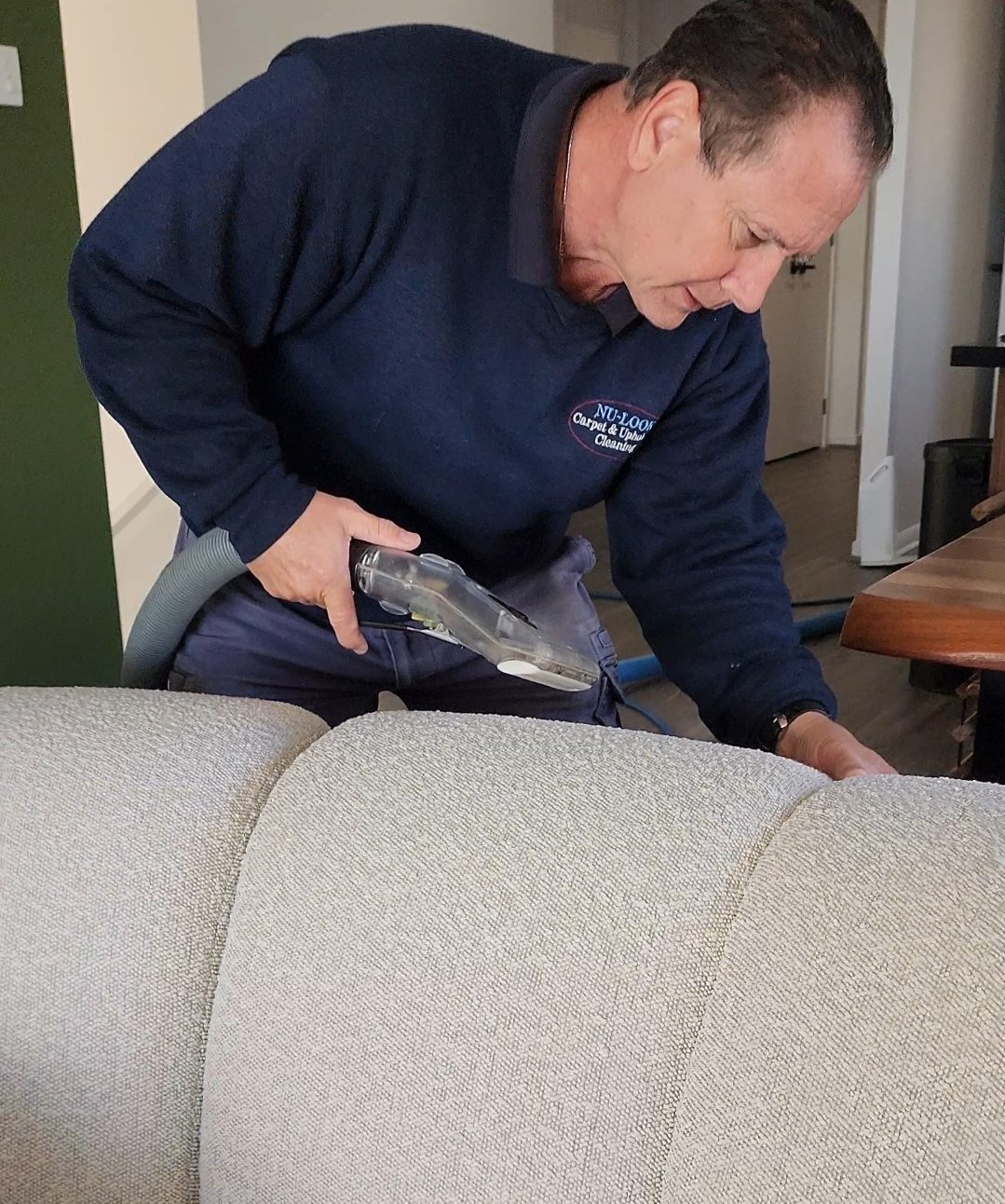 Ian in a Nu-Look shirt cleaning a light fabric lounge with a hand upholstery tool
