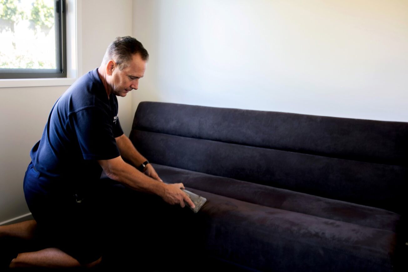 Ian cleaning a dark fabric sofa with a hand upholstery tool